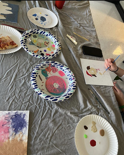 Members of Collab paint canvases and CDs while enjoying pizza at a meeting. 
