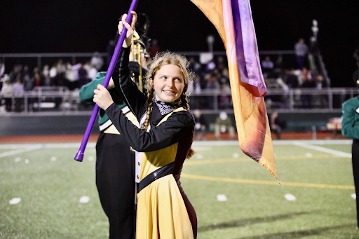 Samantha Eldred holds a purple and orange flag in her color guard uniform while performing at a Ramapo High School football game